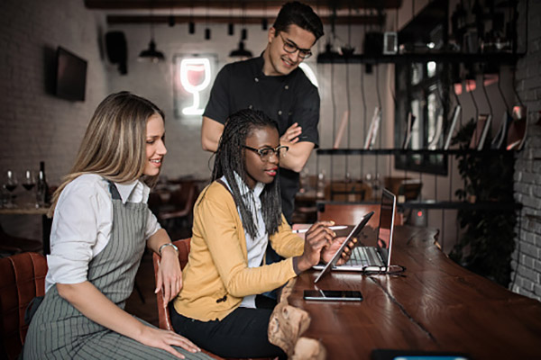A female and a male employee sit at a gastropub table and look on as another woman shares information on her ipad.