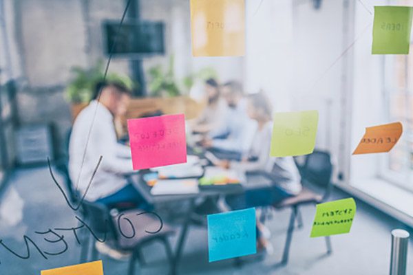 Five young professionals sit around a table in the distance. In the foreground are sticky notes from a recent brainstorm session.